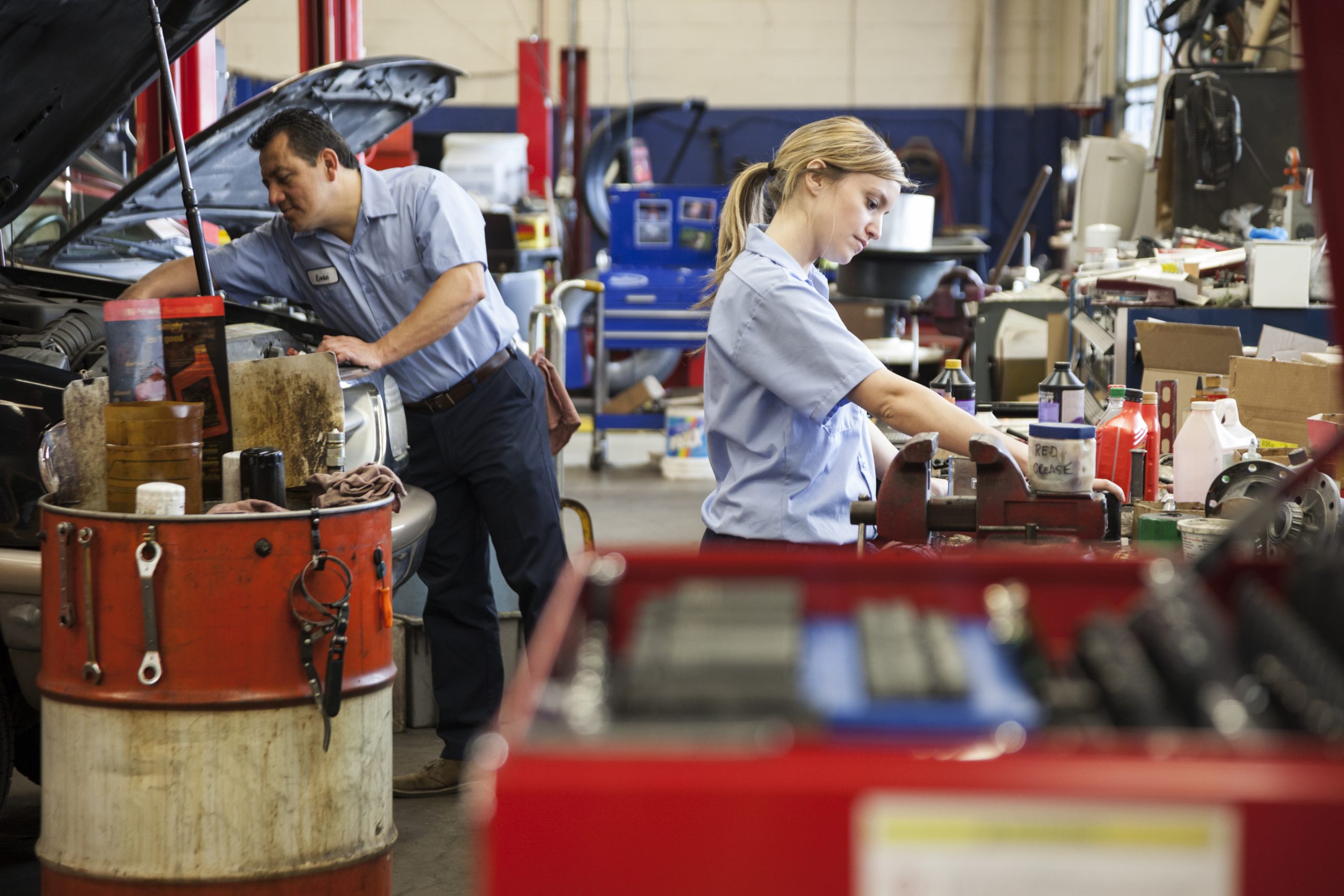 Seattle,United States,Caucasian female mechanic works on engine in auto repair shop with Hispanic coworker in background